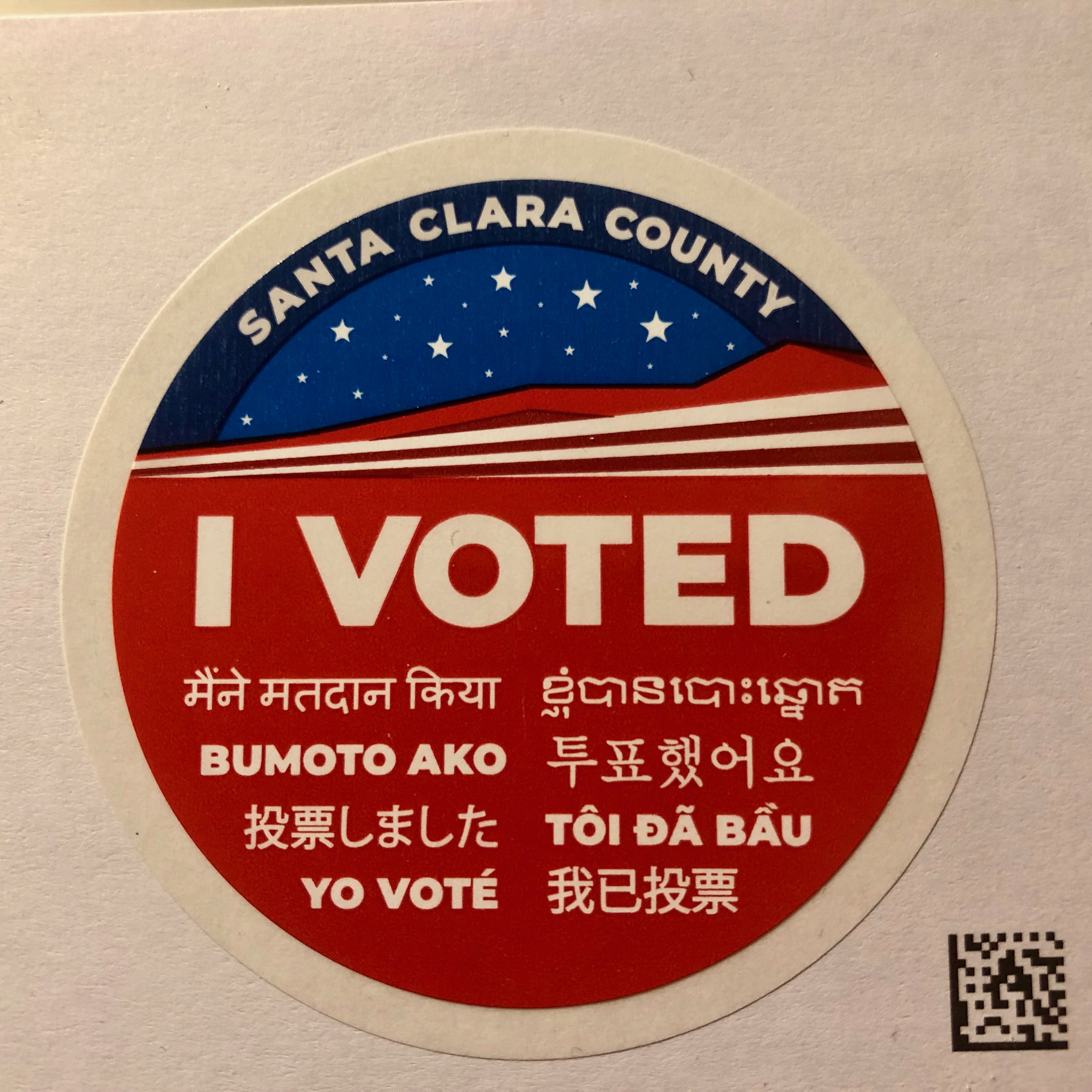 A multilingual I Voted sticker from Santa Clara County resting on a mail ballot envelope