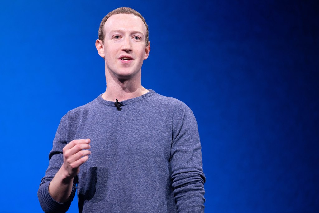 Mark Zuckerberg speaking on stage in a gray sweater against a blue backdrop