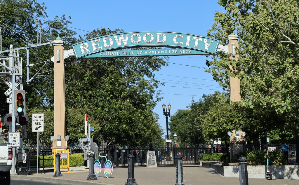 A metal arch over a downtown Redwood City street reading Redwood City, Climate Best by Government Test