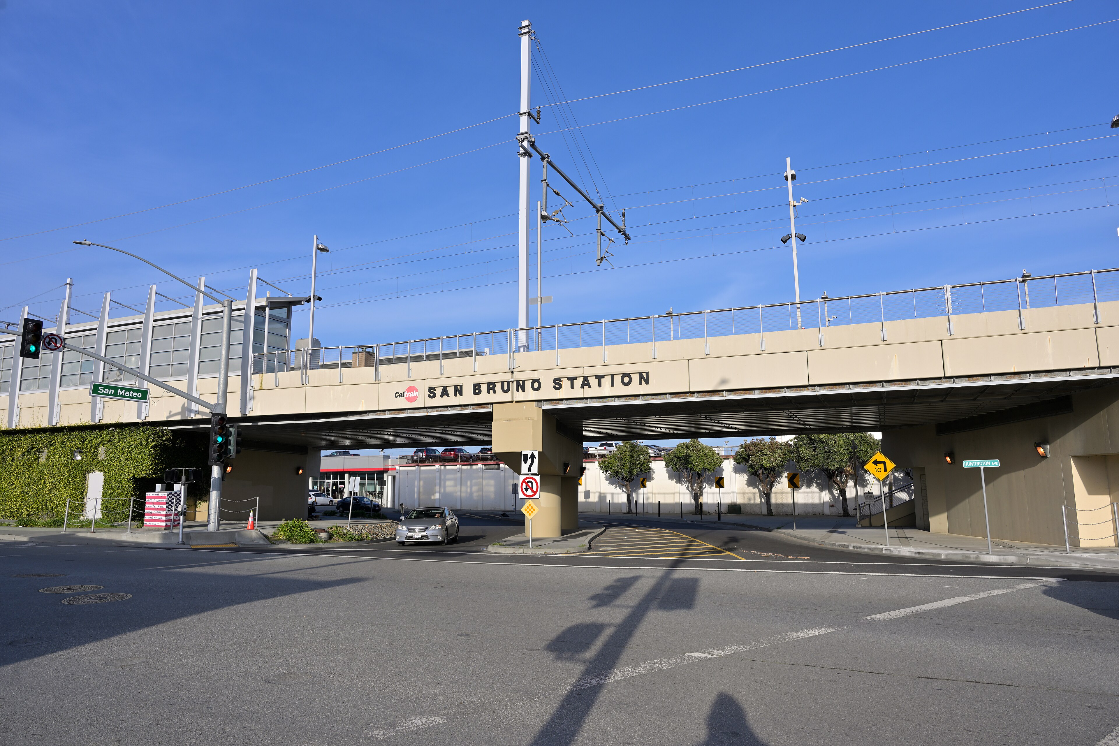 A concrete rail bridge marked San Bruno Station spanning San Bruno Avenue under a blue sky