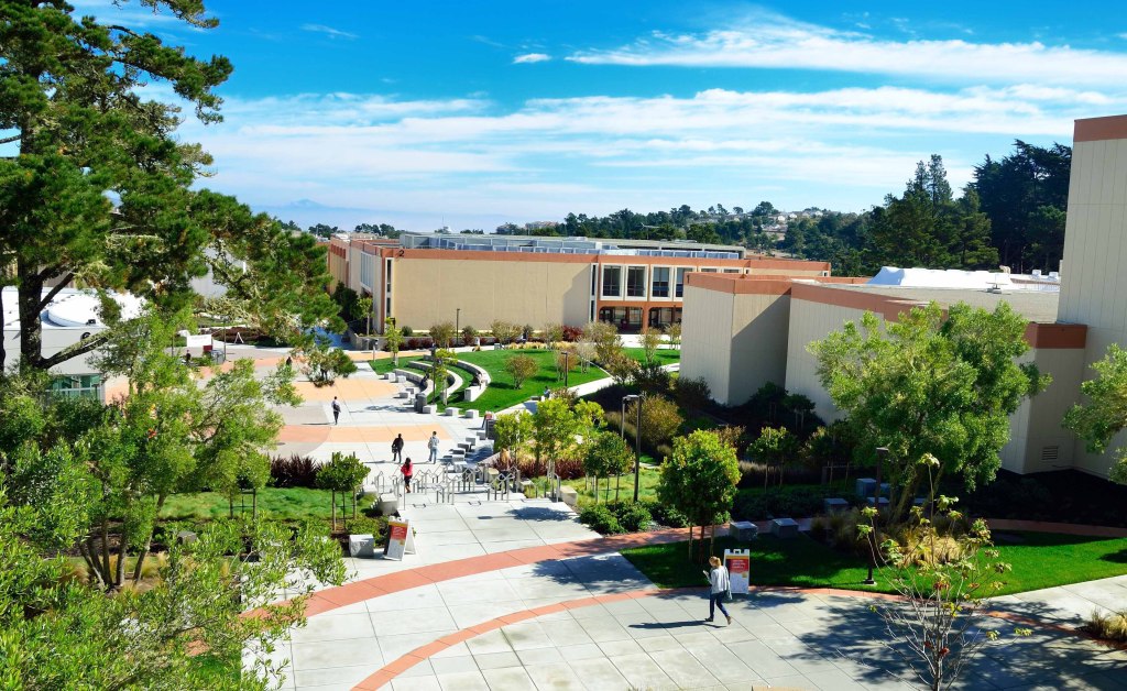 A landscaped college quad with walkways and stucco buildings under a blue sky
