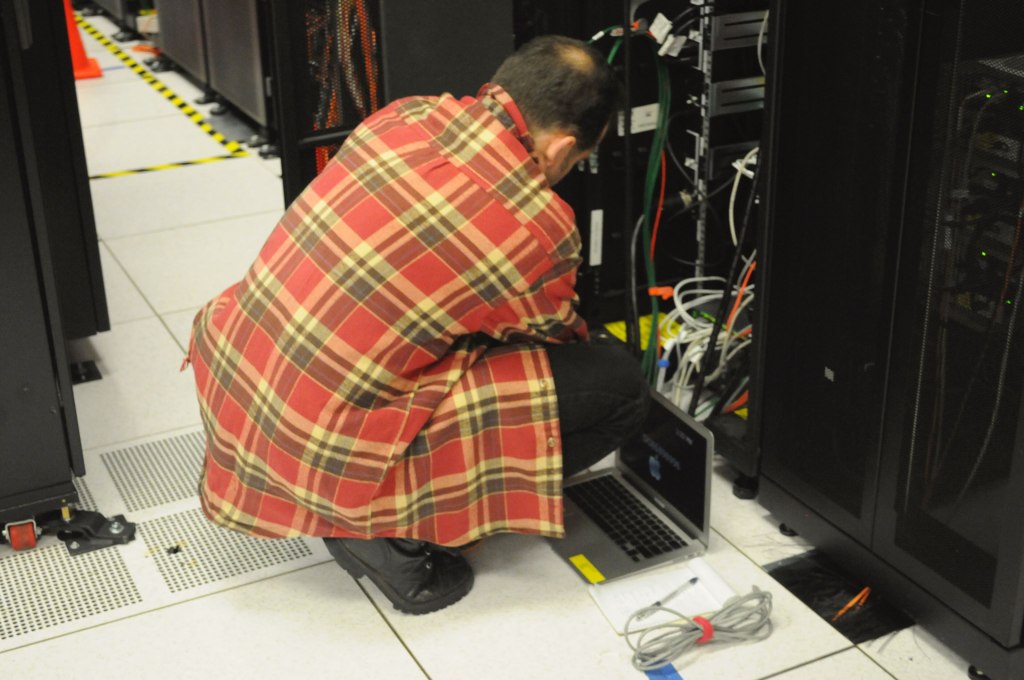 A technician with a laptop working at an open server rack in a data center