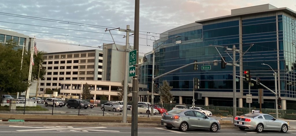 Glass office buildings and a parking lot at a North San Jose intersection with power lines overhead