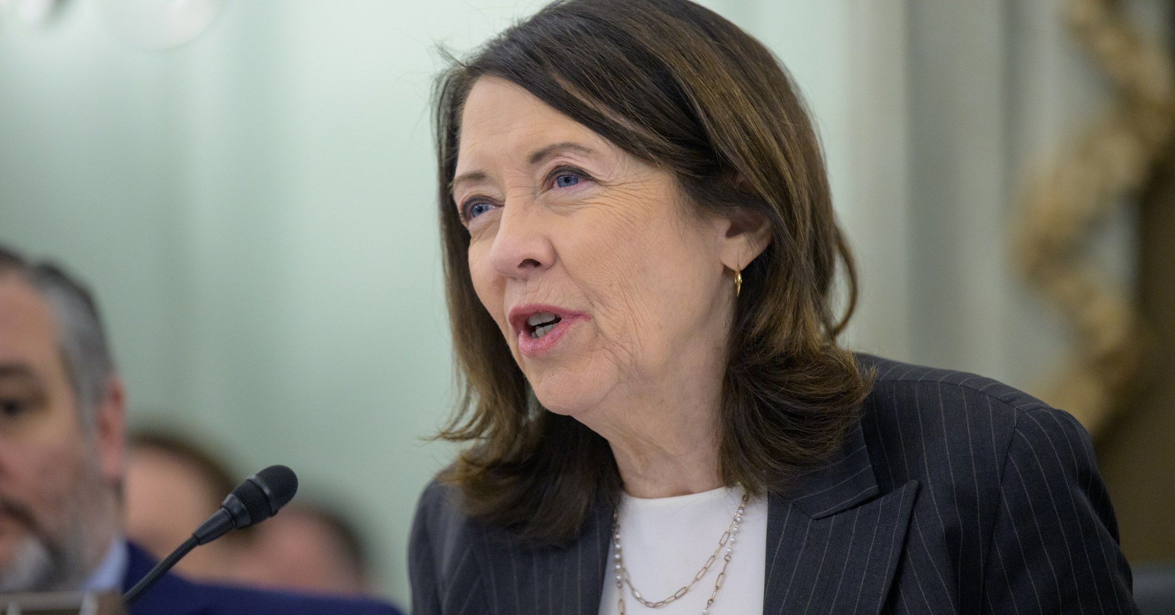 Sen. Maria Cantwell speaks into a microphone at a Senate Commerce Committee hearing, with Sen. Ted Cruz seated in the background.