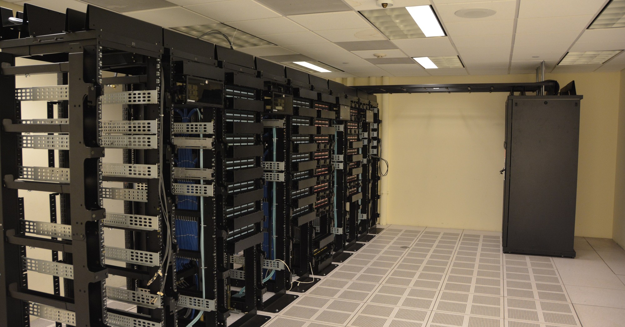 Rows of black server racks with cabling in a white-walled data center room