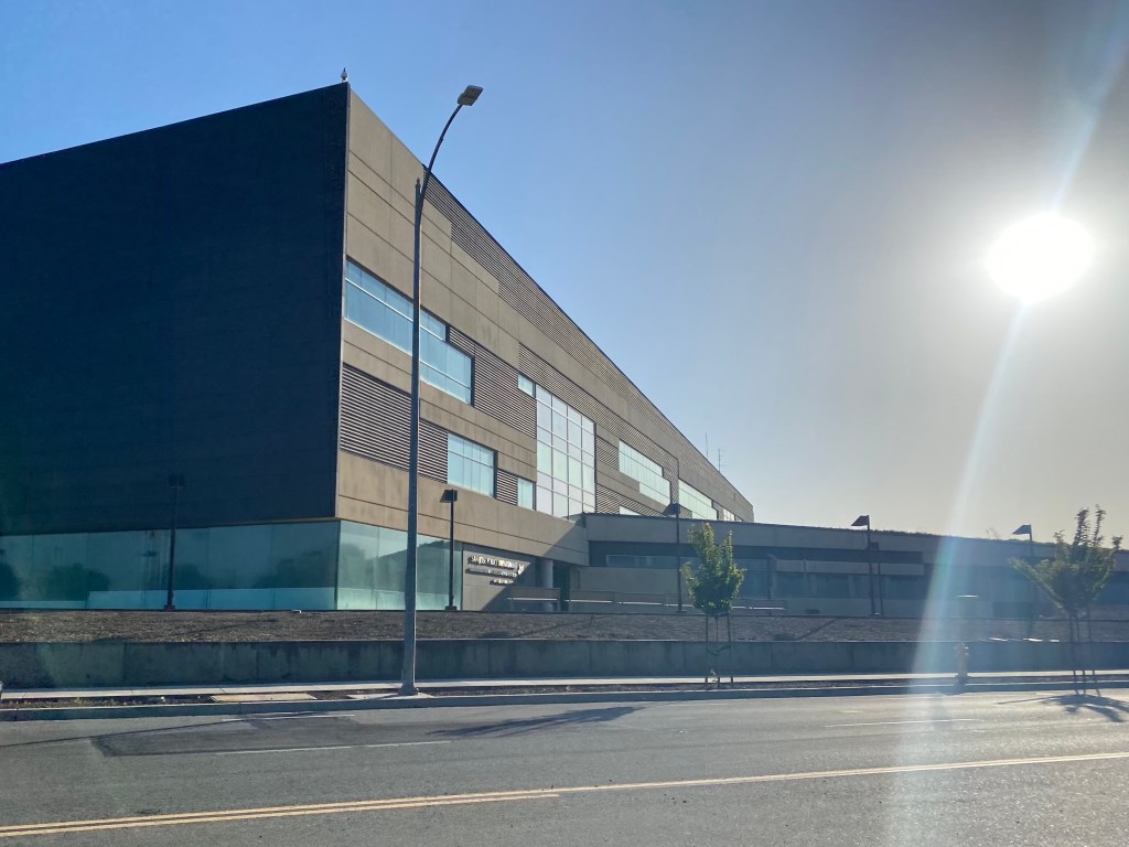 A modern two-story police station building with dark glass panels beside a street in San Jose