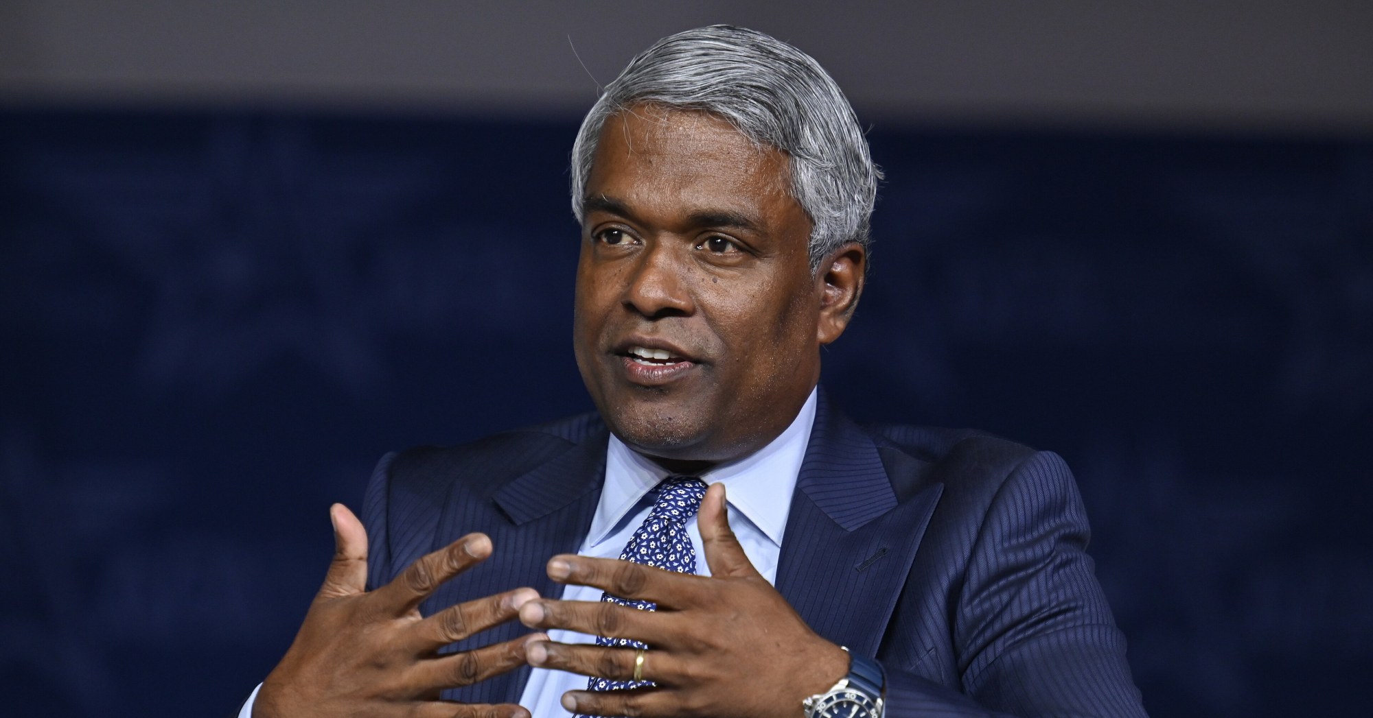 Google Cloud CEO Thomas Kurian, in a dark suit, gestures with both hands while speaking on a panel.